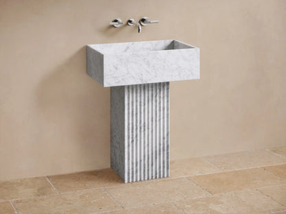 Close-up of white marble rectangular sink with grey veining and a black drain hole, featuring a fluted marble base.