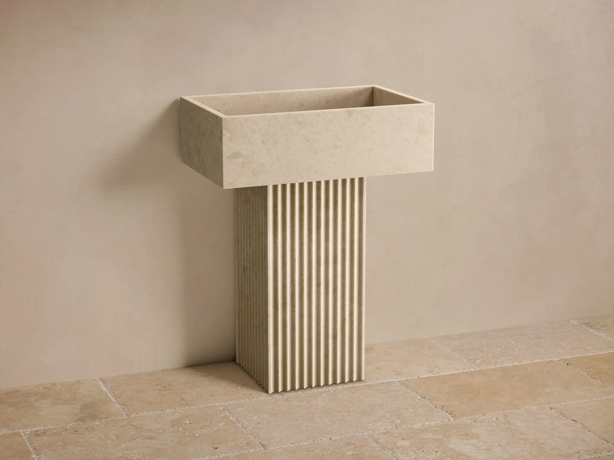Front view of the light beige honed stone Riven Pedestal Sink, featuring a fluted base and an integrated sink basin.