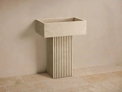 Front view of the light beige honed stone Riven Pedestal Sink, featuring a fluted base and an integrated sink basin.
