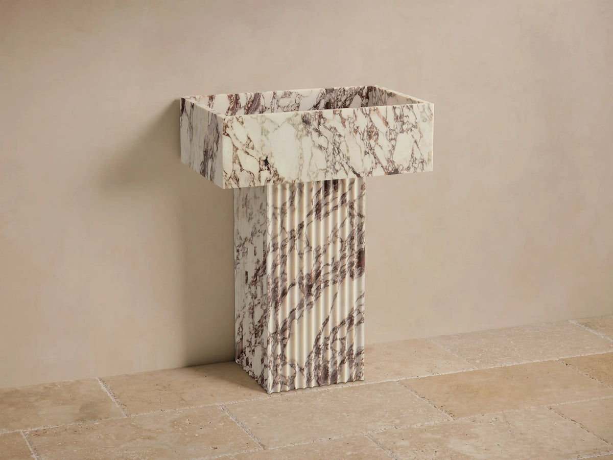 Front view of the white Riven Pedestal Sink, featuring brown-purple veining, a fluted rectangular base, and integrated basin.