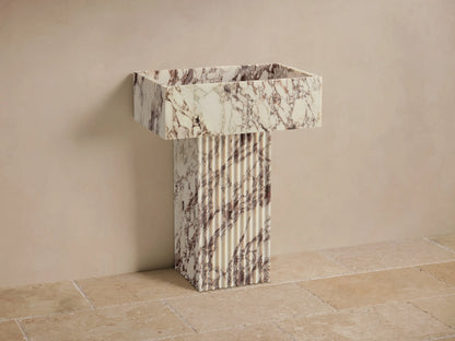 Front view of the white Riven Pedestal Sink, featuring brown-purple veining, a fluted rectangular base, and integrated basin.