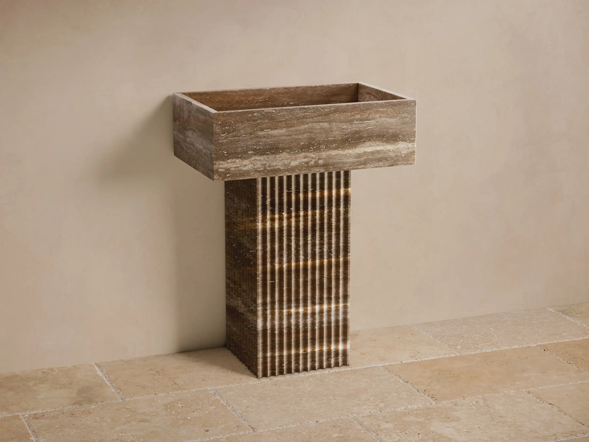 Front view of the Riven Pedestal Sink, crafted from mottled natural brown stone with a fluted pedestal base and integrated basin.