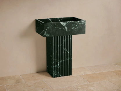 Front view of the dark green marble Riven Pedestal Sink with white veining, a fluted base, and an integrated sink top.