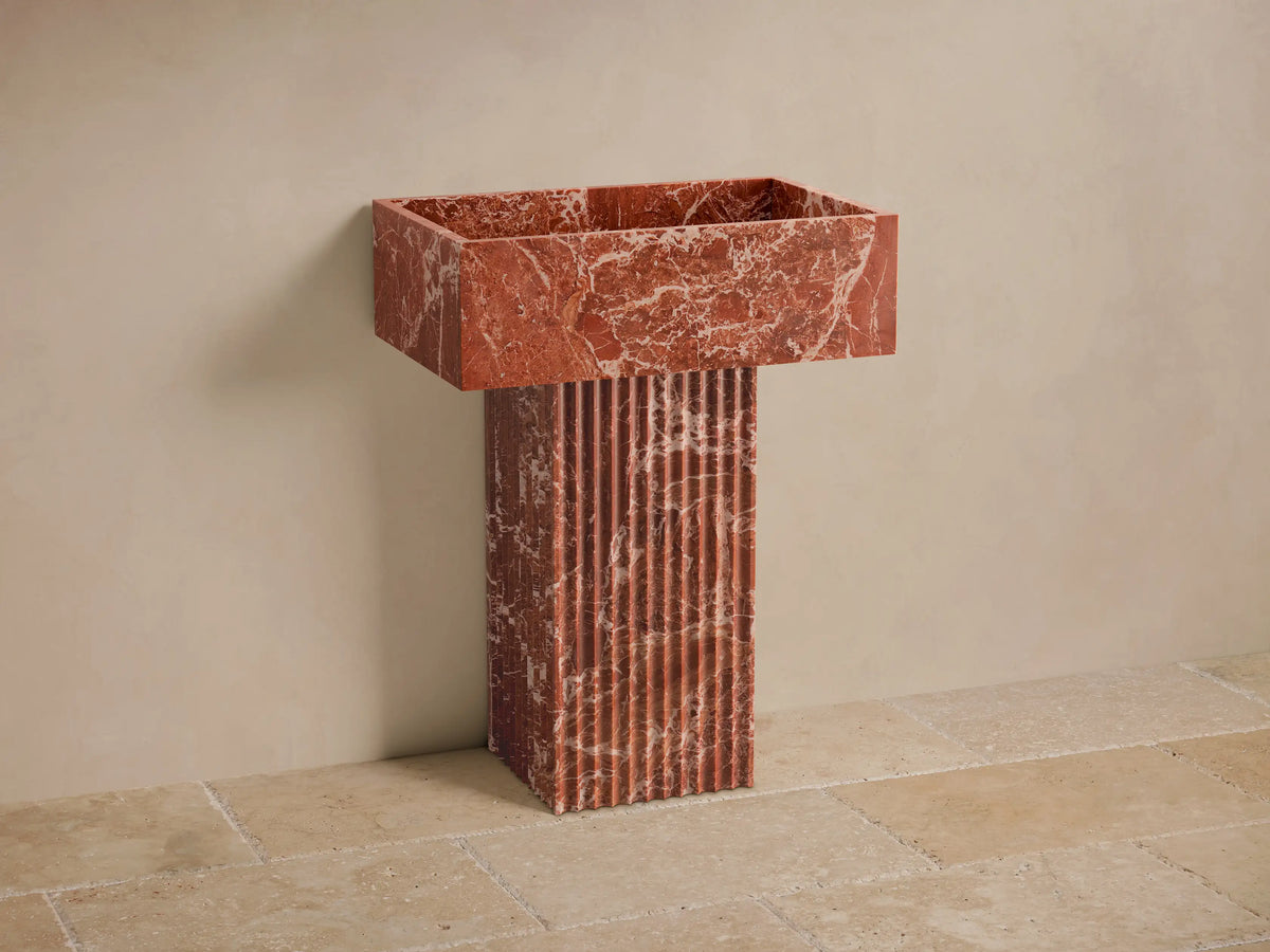 Front view of the red natural stone Riven Pedestal Sink with a fluted base and prominent white veining details.