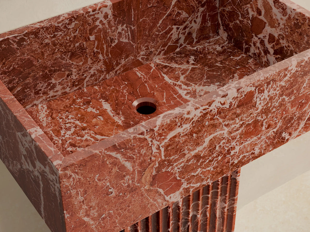 Front view of a red marbled Riven Pedestal Sink with a fluted base and integrated rectangular sink.