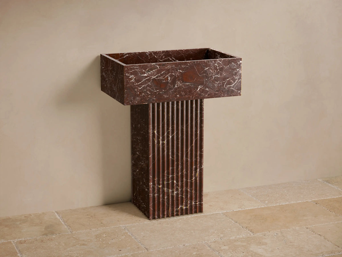 Front view of a reddish-brown marble Riven Pedestal Sink with white veining and a fluted base.