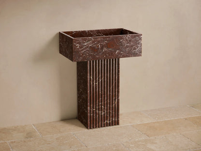 Front view of a reddish-brown marble Riven Pedestal Sink with white veining and a fluted base.