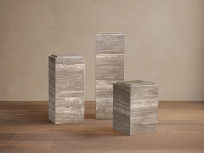 Front view of three rectangular Marmont Pedestals, varying heights, made of greyish-brown natural stone with horizontal veining, on a wood floor.