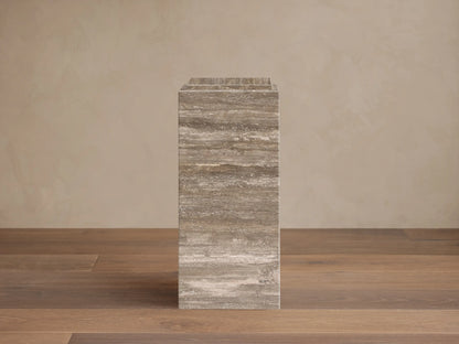 Front view of the brown and gray veined natural stone Marmont Pedestal with a stepped top, standing on a wood floor.