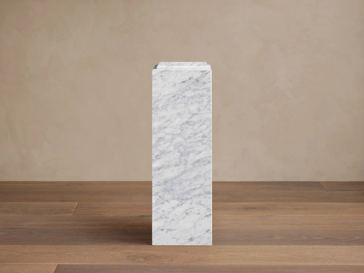 Front view of the white marble Marmont Pedestal with gray veining, standing upright on a wooden floor.