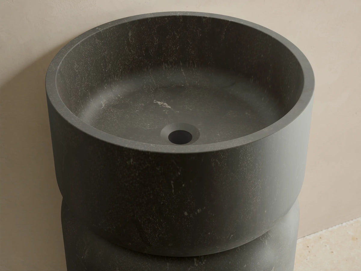 Front view of the dark gray honed stone Vaso Pedestal Sink, featuring a cylindrical base and integrated round basin.