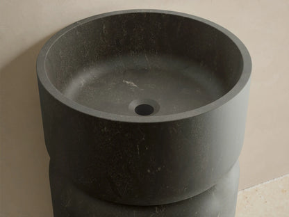 Front view of the dark gray honed stone Vaso Pedestal Sink, featuring a cylindrical base and integrated round basin.
