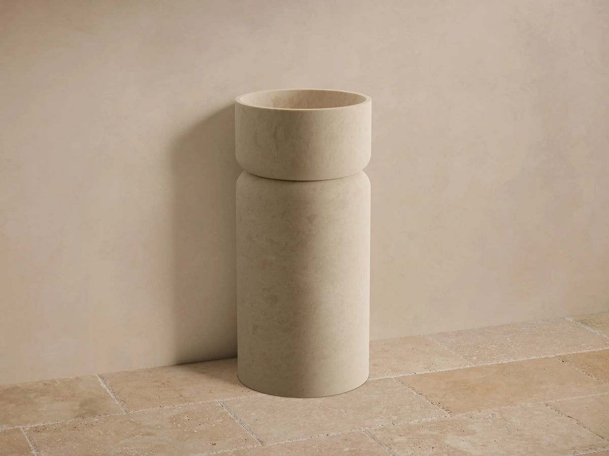 Front view of the natural stone beige Vaso Pedestal Sink, featuring a cylindrical pedestal base and integrated basin.
