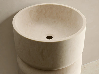 Front view of the light beige Vaso Pedestal Sink, a cylindrical stone base topped with an integrated circular basin.