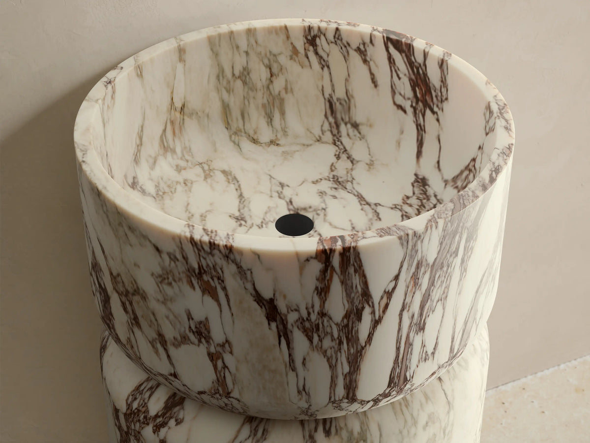 Front view of a white and burgundy veined marble Vaso Pedestal Sink, with a cylindrical pedestal base and integrated bowl.