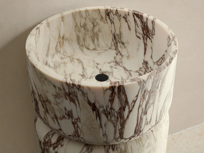 Front view of a white and burgundy veined marble Vaso Pedestal Sink, with a cylindrical pedestal base and integrated bowl.