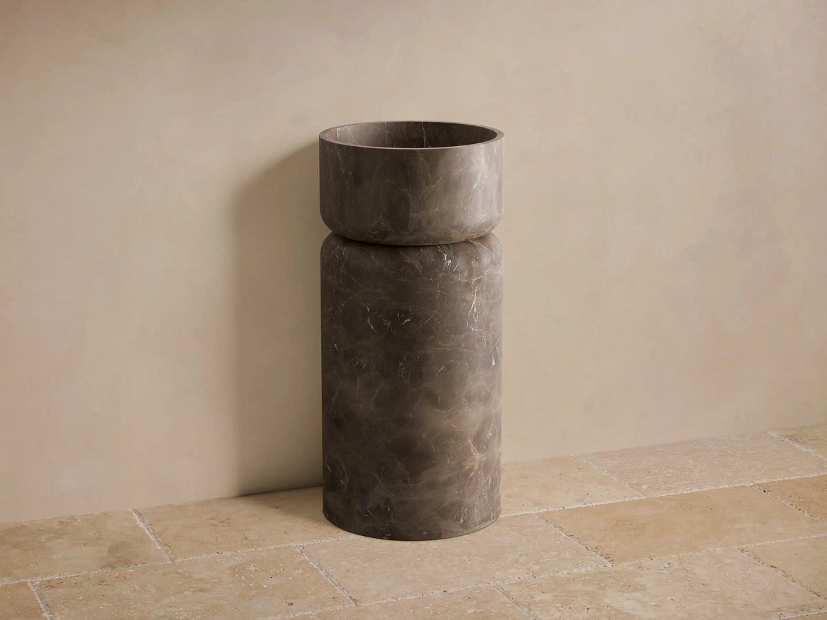 Front view of a dark brown marble Vaso Pedestal Sink, featuring a cylindrical base and integrated basin.