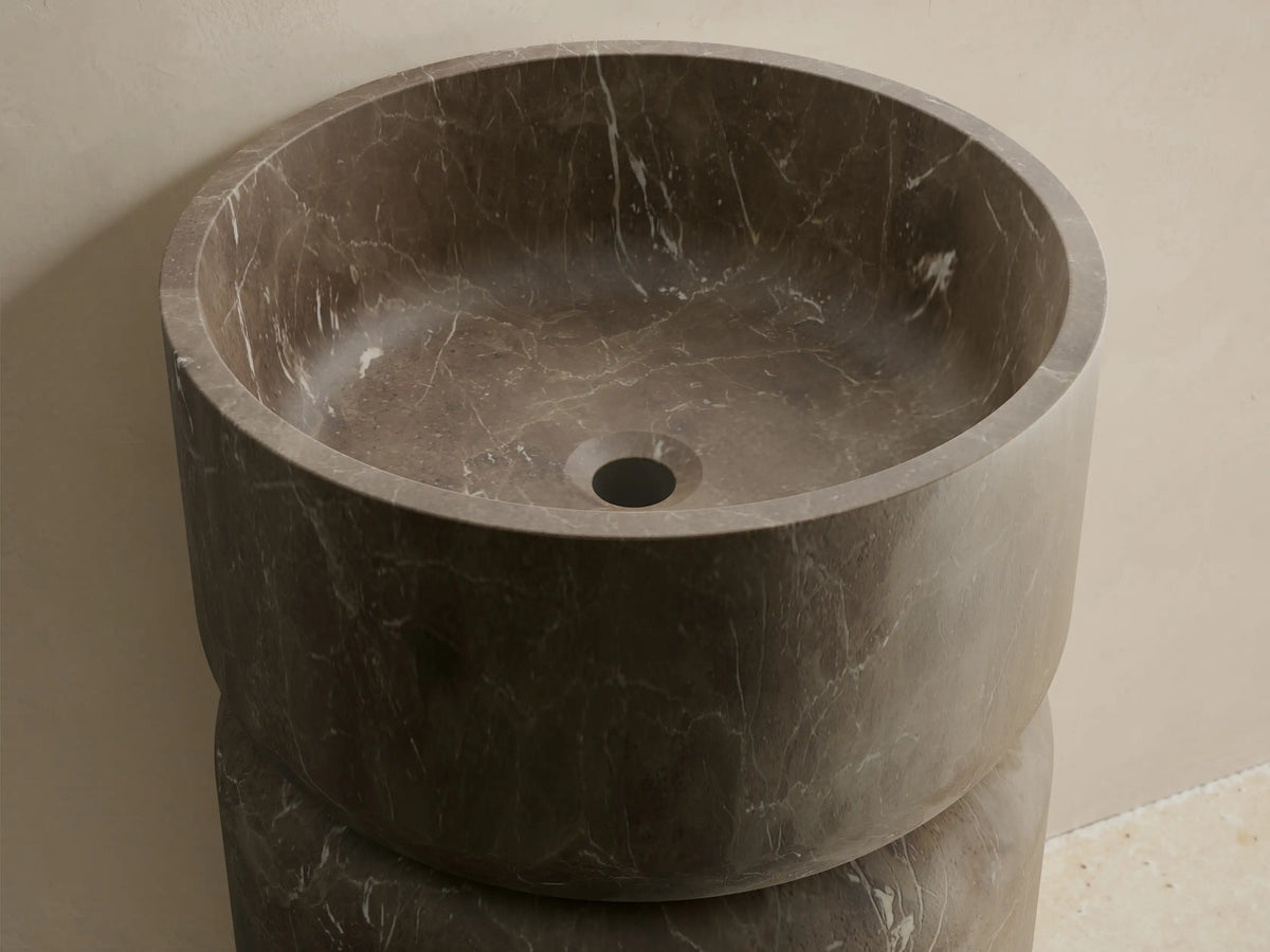 Front view of the dark gray marble Vaso Pedestal Sink, a cylindrical natural stone design with an integrated circular basin and subtle veining.
