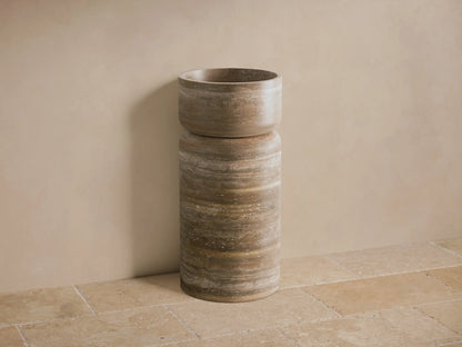 Front view of the cylindrical natural stone Vaso Pedestal Sink with integrated basin, displaying natural brown and beige striations.