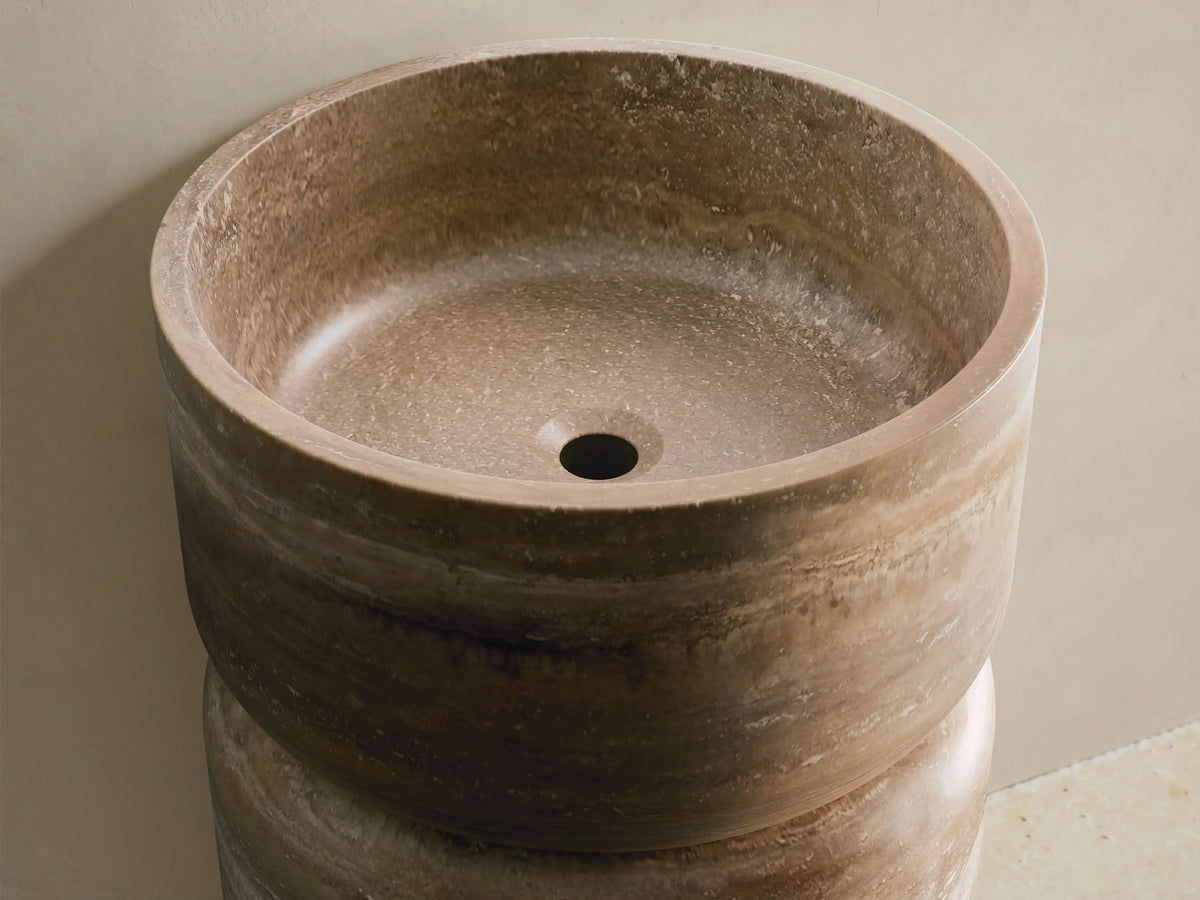 Front view of the cylindrical Vaso Pedestal Sink crafted from natural brown, beige, and gray striated stone, with an integrated basin.