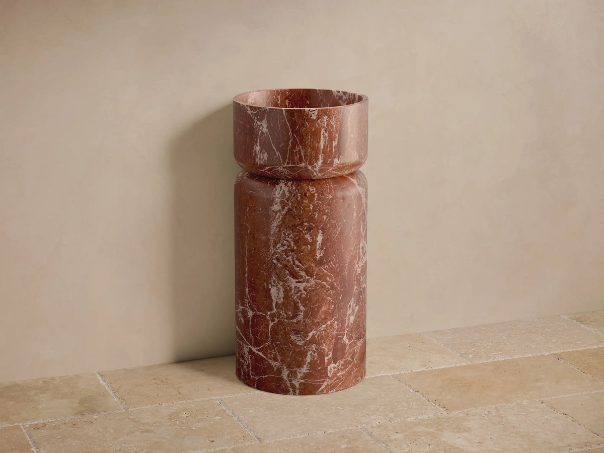 Front view of the red marble Vaso Pedestal Sink, a cylindrical design with an integrated bowl and white veining.