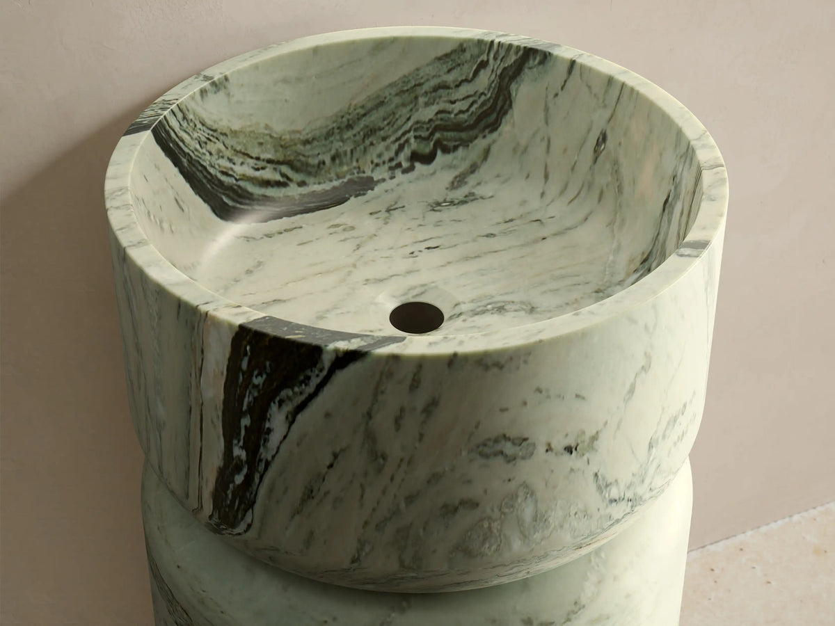 Front view of the green marble Vaso Pedestal Sink, featuring a cylindrical base, integrated bowl top, and natural veining.