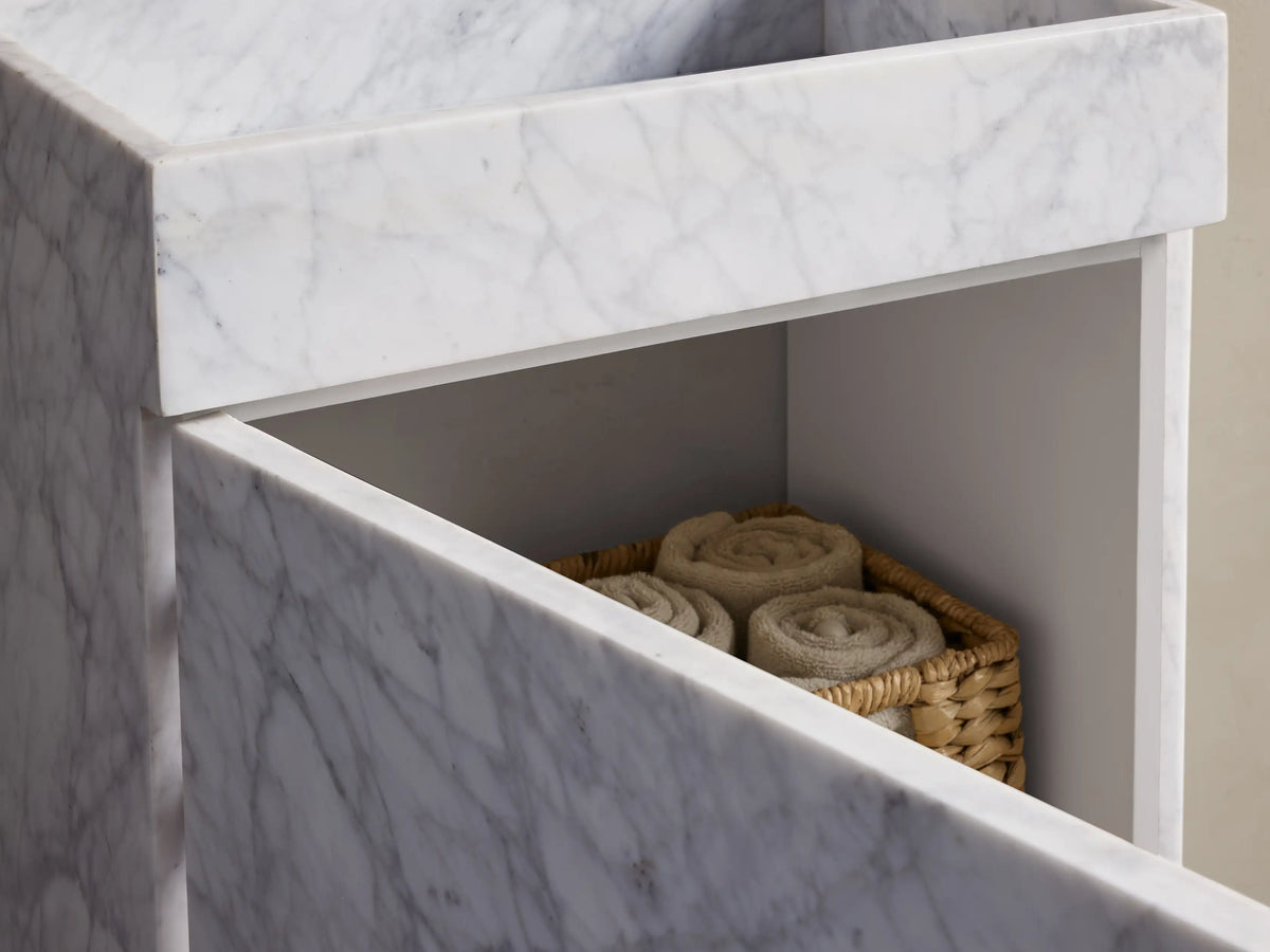 Front view of a white marble pedestal basin with elegant gray veining, featuring a wall-mounted chrome faucet.