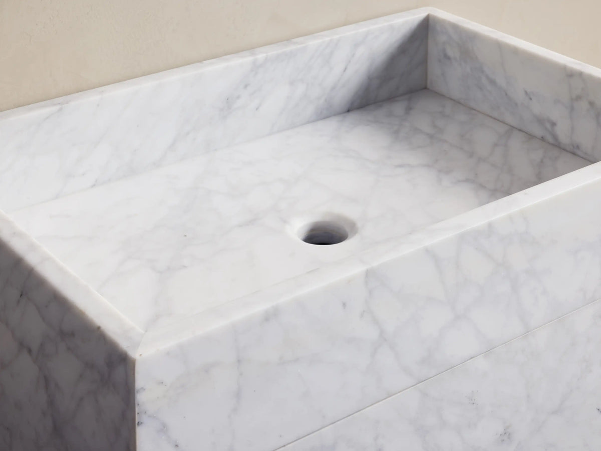 Close-up of partially open drawer of white marble vanity, revealing a wicker basket with three rolled beige towels inside.