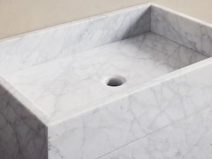 Close-up of partially open drawer of white marble vanity, revealing a wicker basket with three rolled beige towels inside.