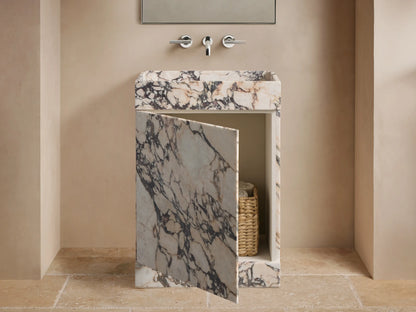Front view of a white marble sink vanity with purple-black veining. Its door is ajar, revealing a woven basket with towels.