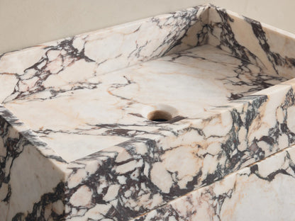 Front view of white Marble Pedestal Sink with black and pink veining and square basin. Chrome wall-mounted faucet.