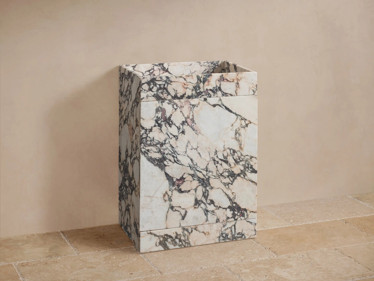 Front view of a white and cream marble pedestal sink with prominent black and reddish-brown veining and a rectangular basin.