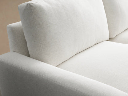 Remington Sofa, 2-seater, light grey fabric, modern design, thick cushions, square arms, on a wooden floor against a beige wall.