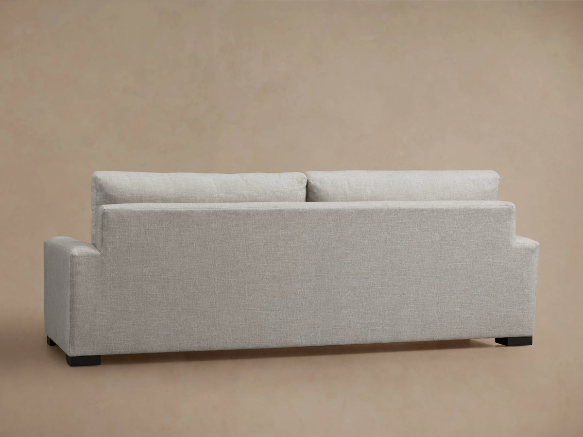 Remington Sofa, back view. Light gray textured fabric, two loose back cushions, square arms, dark feet, on beige background.
