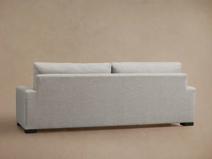 Remington Sofa, back view. Light gray textured fabric, two loose back cushions, square arms, dark feet, on beige background.