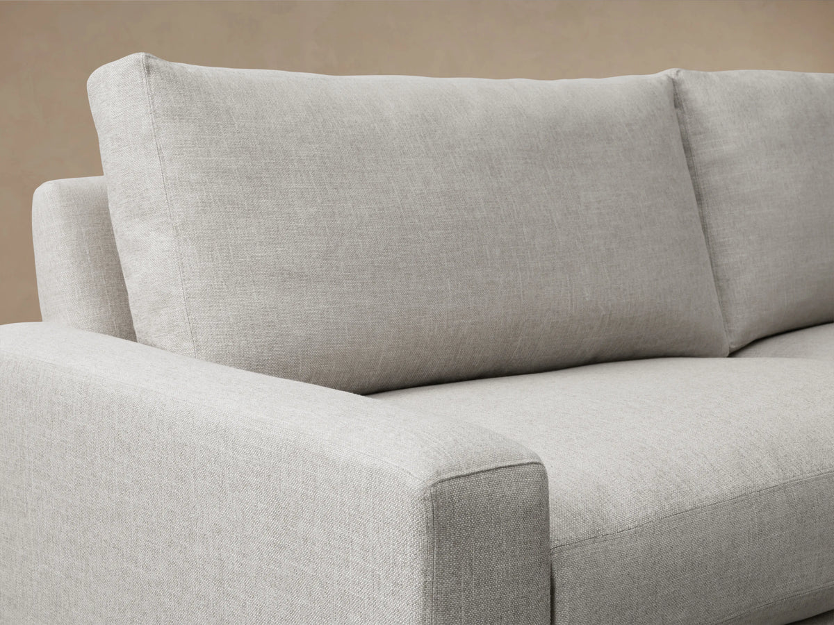 Close-up of a light gray Remington Sofa, showing a square armrest, two plush back cushions, and textured fabric.