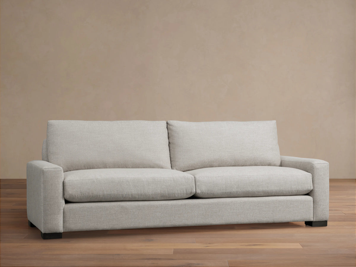Front view of a light gray Remington Sofa with two seat cushions, two back cushions, and wide arms, on a wooden floor.