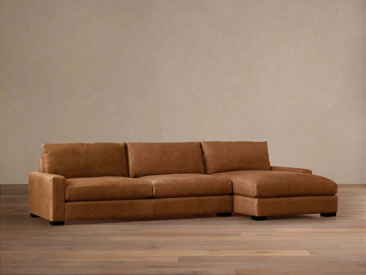 Remington Two-Piece Chaise Sectional in warm brown leather, chaise on right, in a room with light wall and wood floor.