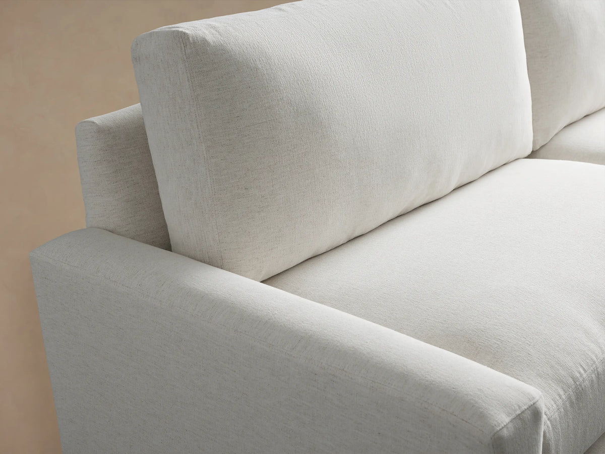 Plush white fabric Remington Sofa, a two-seater with wide square arms & dark legs, angled in a room with a tan wall & wood floor.