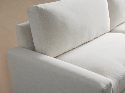 Plush white fabric Remington Sofa, a two-seater with wide square arms & dark legs, angled in a room with a tan wall & wood floor.