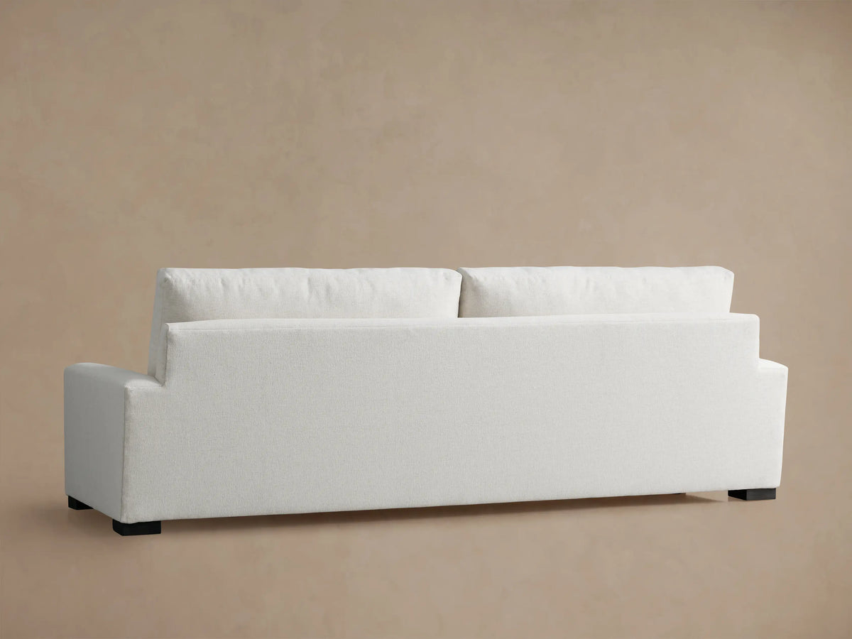 Close-up of a light-colored, textured Remington Sofa armrest, seat, and plush back cushion against a warm beige background.