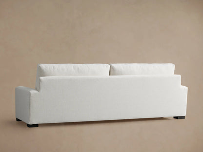 Close-up of a light-colored, textured Remington Sofa armrest, seat, and plush back cushion against a warm beige background.
