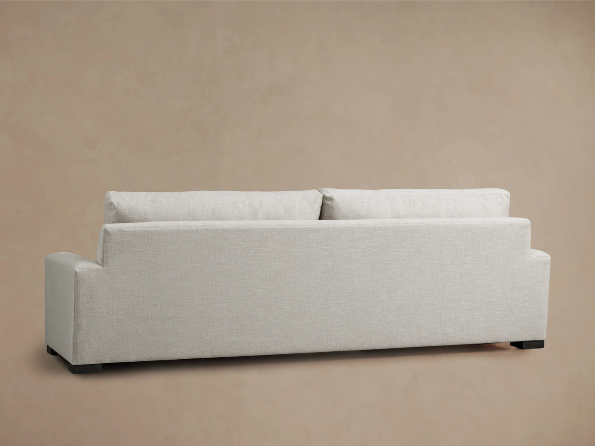 Remington Sofa: Light oatmeal textured fabric, two-cushion sofa with broad arms on a wood floor against a tan wall.