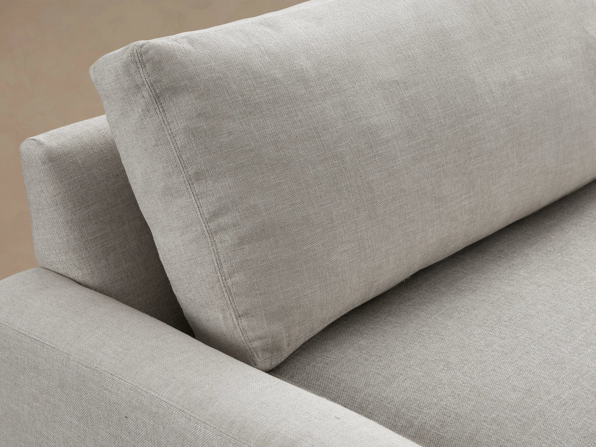 Remington Sofa: light gray textured fabric, 2 plump seat & back cushions, wide square arms, dark feet, on a wood floor.