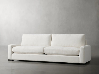 Remington Sofa, modern off-white 2-seater with wide square arms and dark base, centered against a plain gray wall.