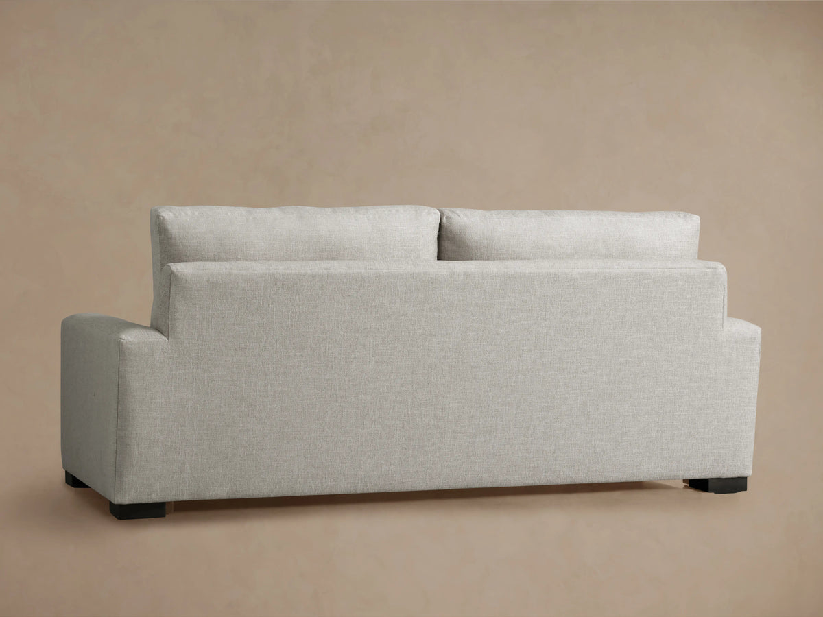 Back view of a light gray Remington sofa with textured fabric, two separate back cushions, wide arms, and dark feet.