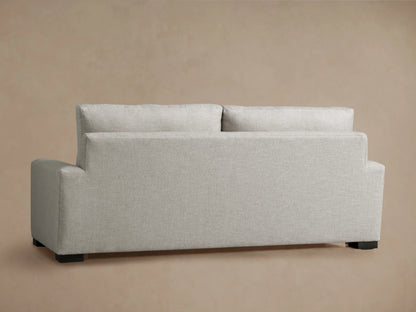 Back view of a light gray Remington sofa with textured fabric, two separate back cushions, wide arms, and dark feet.