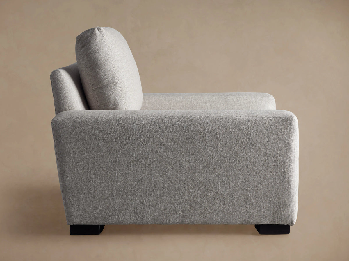 Side view of the light gray upholstered Remington Chair, featuring a back cushion and dark block feet.