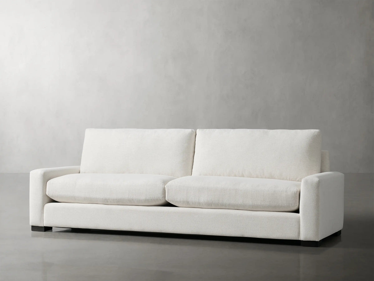 Front view of Remington Sofa, a modern two-seater with textured light cream fabric, plump cushions, and straight block arms.