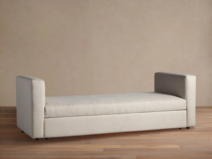 Light beige Remington Trundle Sleeper Daybed with two low, rounded armrests, on a wooden floor against a beige wall.